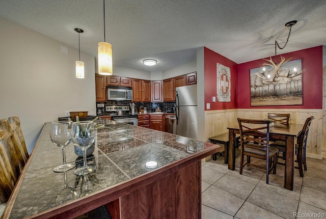 405 Four Oclock Rd Unit 15-A, Breckenridge, CO 80424 - kitchen featuring tile counters, appliances with stainless steel finishes, a wainscoted wall, a peninsula, and decorative light fixtures