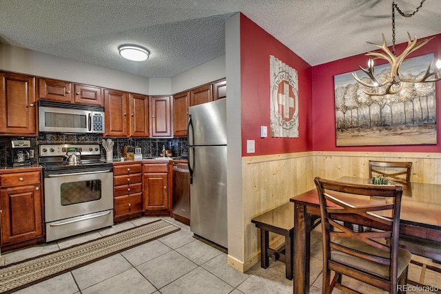 405 Four Oclock Rd Unit 15-A, Breckenridge, CO 80424 - kitchen featuring stainless steel appliances, wood walls, a textured ceiling, wainscoting, and brown cabinetry