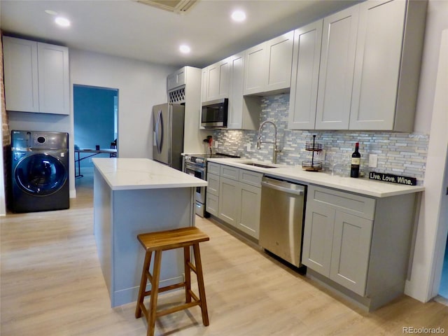 kitchen with washer / clothes dryer, a center island, a sink, light wood finished floors, and appliances with stainless steel finishes