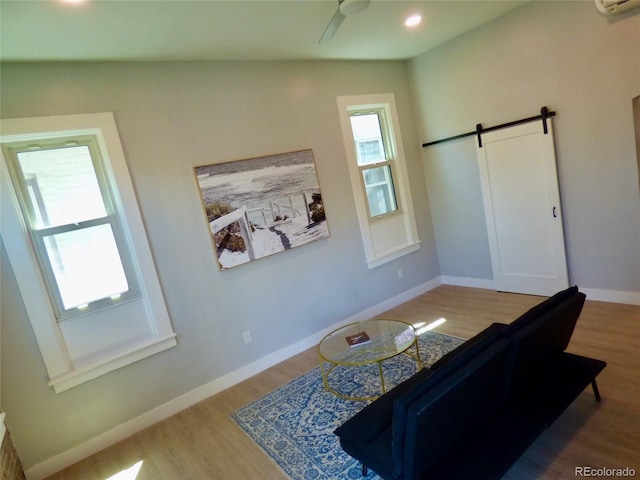 interior space with a ceiling fan, a wall mounted AC, a barn door, wood finished floors, and baseboards