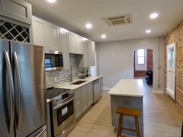 kitchen featuring brick wall, appliances with stainless steel finishes, a sink, and light wood-style floors