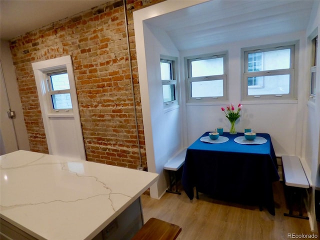 dining area featuring brick wall, a healthy amount of sunlight, and light wood-style flooring