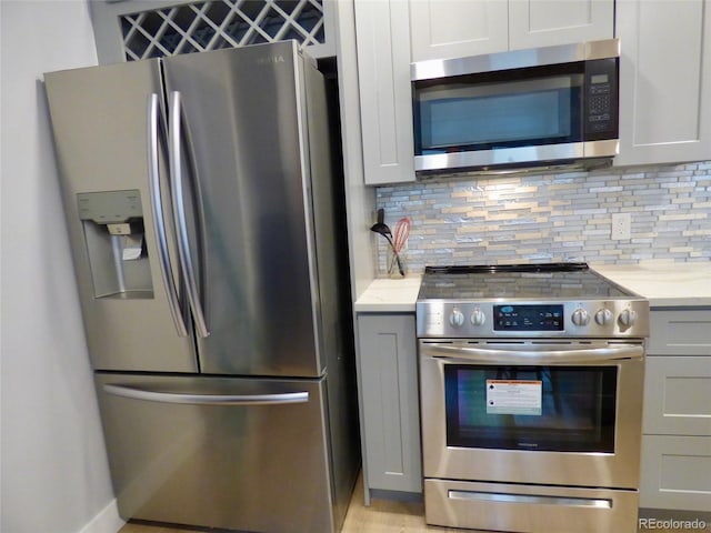 kitchen featuring light stone countertops, appliances with stainless steel finishes, gray cabinets, and tasteful backsplash