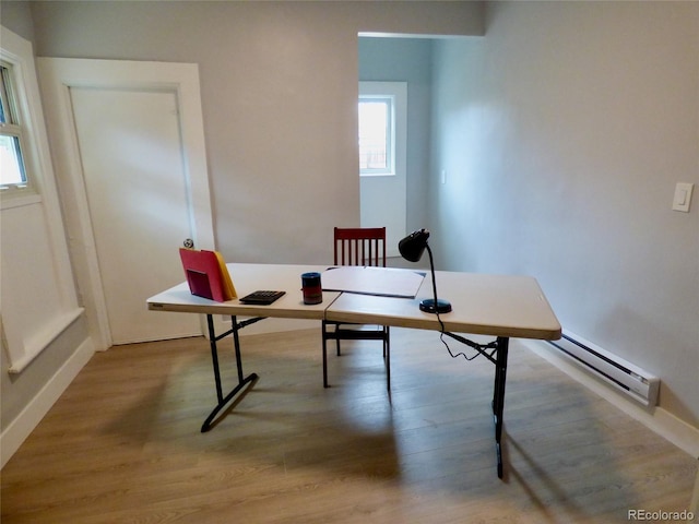 office space with baseboards, a baseboard heating unit, wood finished floors, and a wealth of natural light