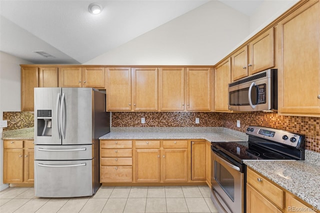 kitchen with appliances with stainless steel finishes, lofted ceiling, light stone countertops, and light tile patterned floors