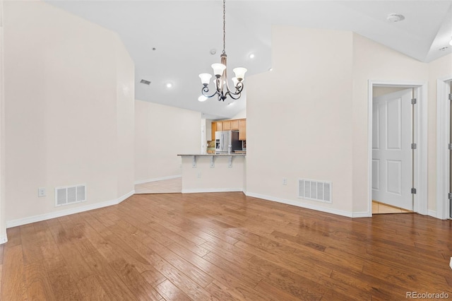 unfurnished living room with hardwood / wood-style flooring, a chandelier, and high vaulted ceiling