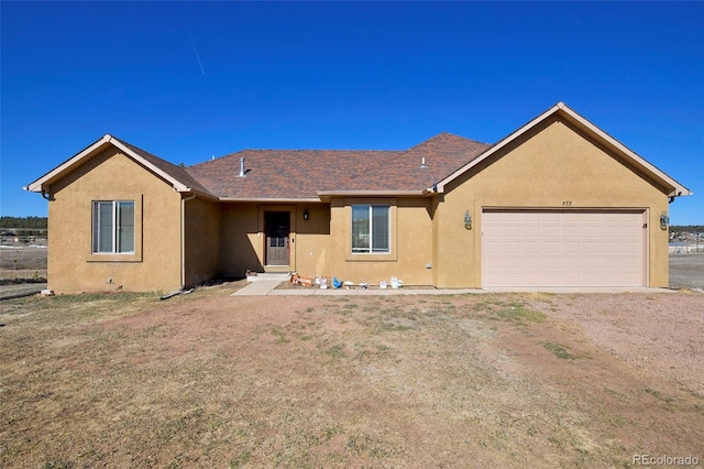 single story home featuring roof with shingles, dirt driveway, an attached garage, and stucco siding