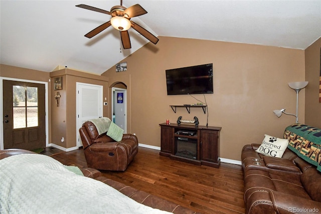 living room featuring baseboards, arched walkways, dark wood finished floors, a ceiling fan, and vaulted ceiling with beams