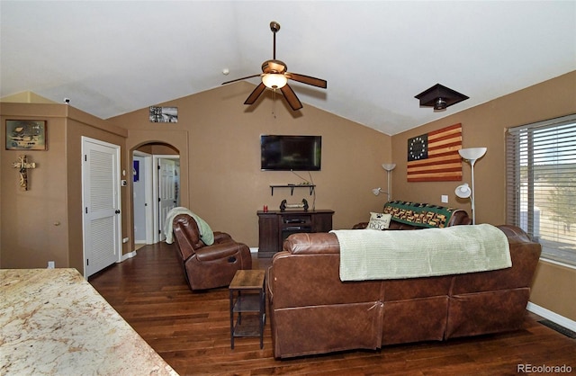 living area with baseboards, arched walkways, a ceiling fan, dark wood-style floors, and vaulted ceiling