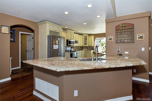 kitchen featuring cream cabinetry, stainless steel appliances, glass insert cabinets, a sink, and a peninsula