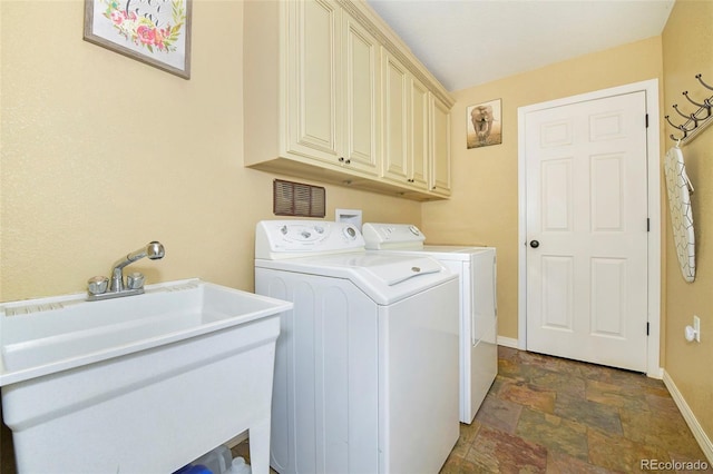 laundry area featuring washing machine and clothes dryer, cabinet space, stone finish flooring, a sink, and baseboards