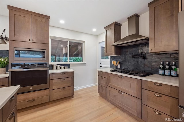 3384 W Arlington Ave, Littleton, CO 80123 - kitchen with wall chimney exhaust hood, appliances with stainless steel finishes, light wood-style flooring, decorative backsplash, and light countertops