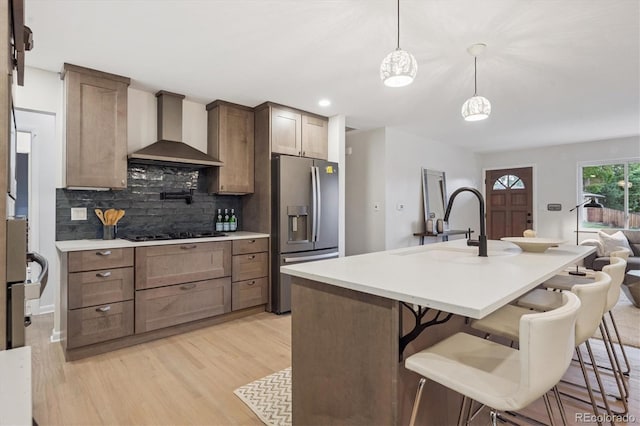 3384 W Arlington Ave, Littleton, CO 80123 - kitchen with stainless steel refrigerator with ice dispenser, wall chimney range hood, light wood-style floors, tasteful backsplash, and a breakfast bar