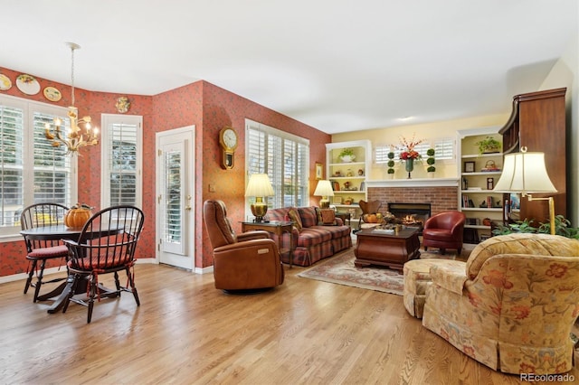 living room with a notable chandelier, a healthy amount of sunlight, light wood-type flooring, and a fireplace