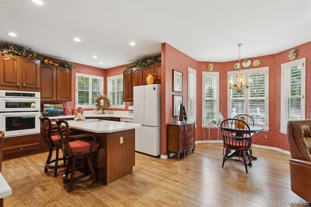 kitchen with a wealth of natural light, pendant lighting, light wood-type flooring, and white appliances