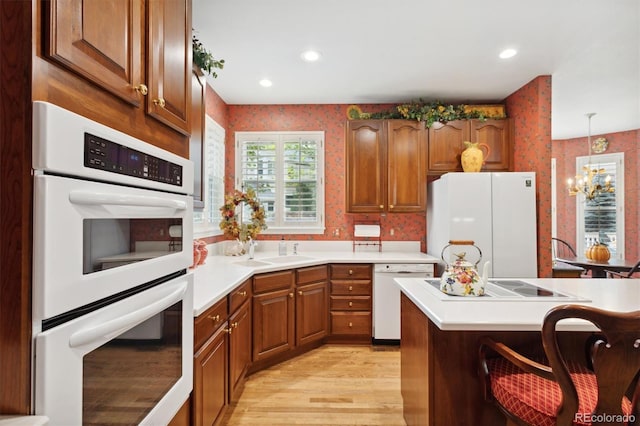 kitchen featuring white appliances, sink, light wood-type flooring, decorative light fixtures, and an inviting chandelier