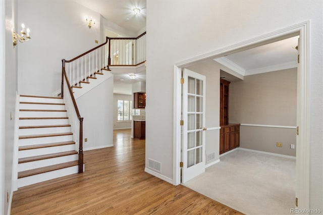 foyer entrance with a high ceiling, visible vents, stairway, light wood finished floors, and crown molding