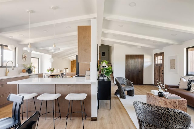 kitchen with kitchen peninsula, sink, light hardwood / wood-style flooring, vaulted ceiling with beams, and hanging light fixtures