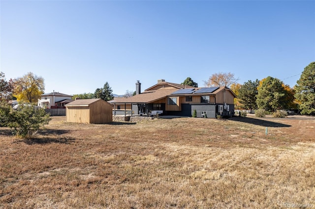 rear view of house with solar panels, a shed, and a lawn