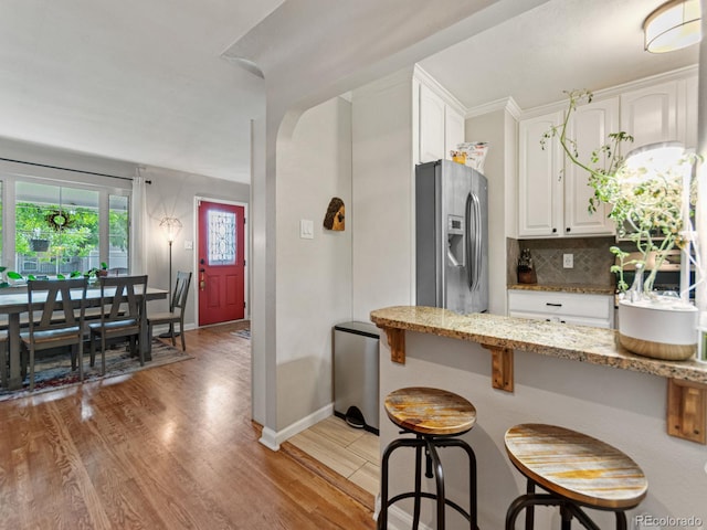 4540 Yarrow St, Wheat Ridge, CO 80033 - kitchen featuring stainless steel fridge with ice dispenser, white cabinets, a kitchen bar, and light stone countertops