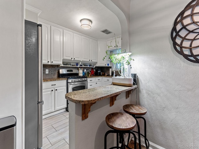 4540 Yarrow St, Wheat Ridge, CO 80033 - kitchen featuring stainless steel appliances, tasteful backsplash, a kitchen bar, white cabinets, and a textured wall