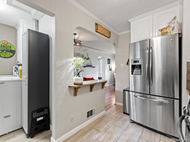 4540 Yarrow St, Wheat Ridge, CO 80033 - kitchen featuring stainless steel fridge with ice dispenser, arched walkways, wood tiled floors, white cabinetry, and crown molding