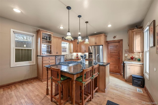 kitchen with sink, decorative backsplash, hanging light fixtures, stainless steel appliances, and a center island with sink