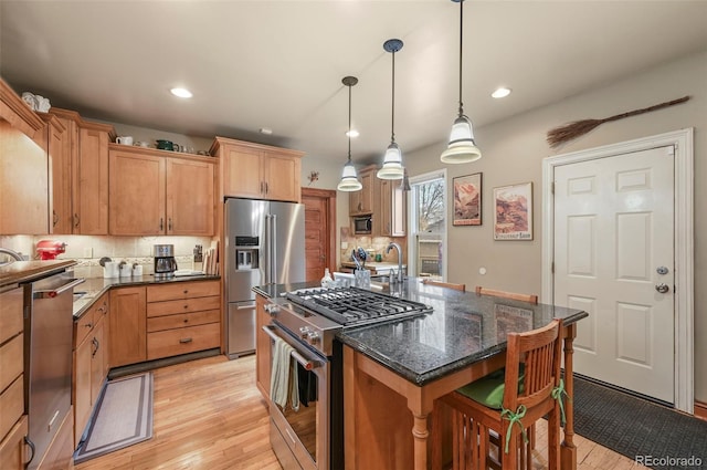 kitchen featuring decorative light fixtures, light wood-type flooring, appliances with stainless steel finishes, a kitchen island, and dark stone counters