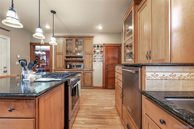 kitchen featuring hanging light fixtures, dark stone countertops, stainless steel range with gas cooktop, light hardwood / wood-style floors, and decorative backsplash