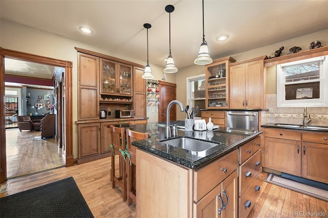 kitchen featuring dark stone counters, decorative light fixtures, sink, and a center island with sink