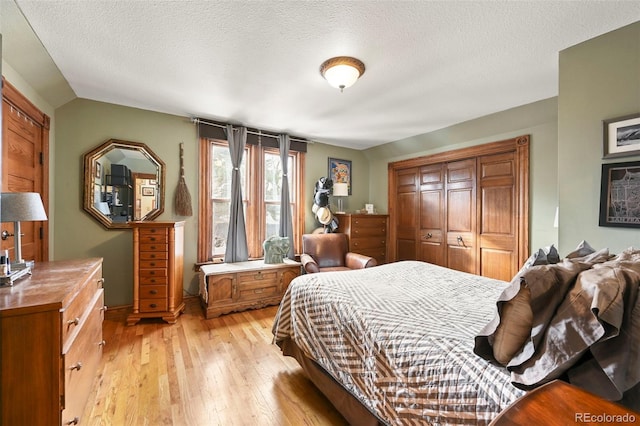 bedroom featuring vaulted ceiling, a closet, a textured ceiling, and light hardwood / wood-style flooring