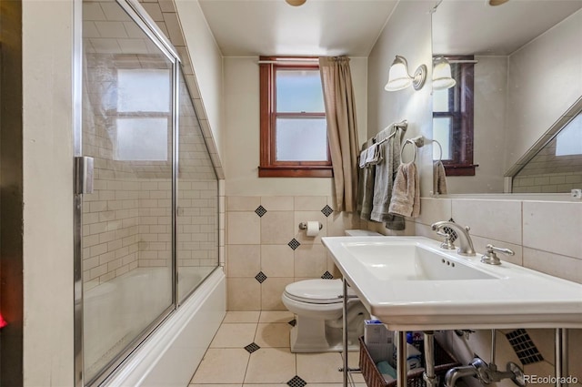 bathroom with tile patterned flooring, combined bath / shower with glass door, tile walls, and toilet