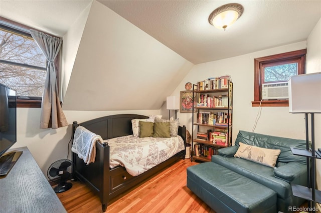 bedroom featuring cooling unit, lofted ceiling, a textured ceiling, and light wood-type flooring