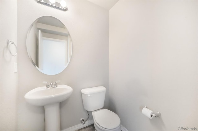 half bathroom featuring toilet, baseboards, and a sink