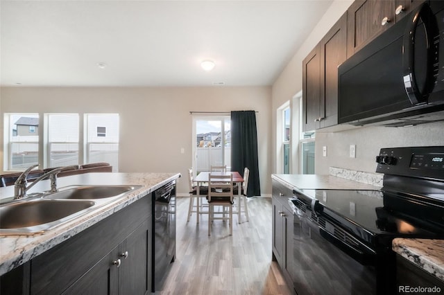 kitchen featuring baseboards, light countertops, a sink, light wood finished floors, and black appliances