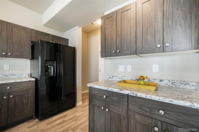 kitchen with dark brown cabinetry, black refrigerator with ice dispenser, light stone counters, and light wood-style floors