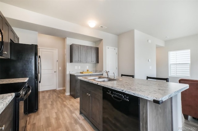 kitchen featuring a sink, light wood-style floors, visible vents, a center island with sink, and black appliances