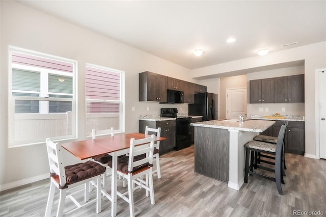 kitchen with light wood-style floors, a kitchen breakfast bar, dark brown cabinetry, and black appliances