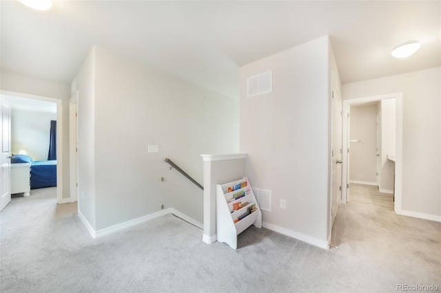 hall with baseboards, visible vents, carpet flooring, and an upstairs landing