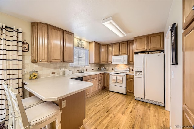 kitchen featuring a breakfast bar, sink, light wood-type flooring, kitchen peninsula, and white appliances