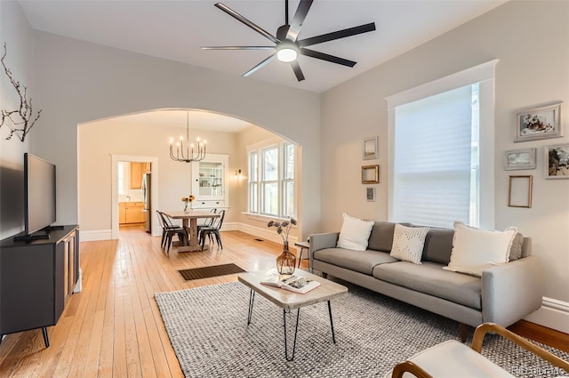 living room with baseboards, arched walkways, ceiling fan with notable chandelier, and light wood finished floors