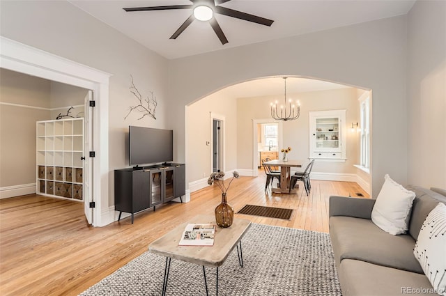 living area featuring light wood-type flooring, arched walkways, baseboards, and ceiling fan with notable chandelier