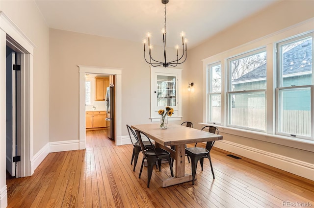 dining space with an inviting chandelier, light wood-style floors, visible vents, and baseboards