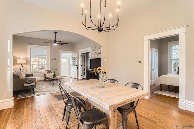 dining space with baseboards, light wood-type flooring, arched walkways, and a healthy amount of sunlight