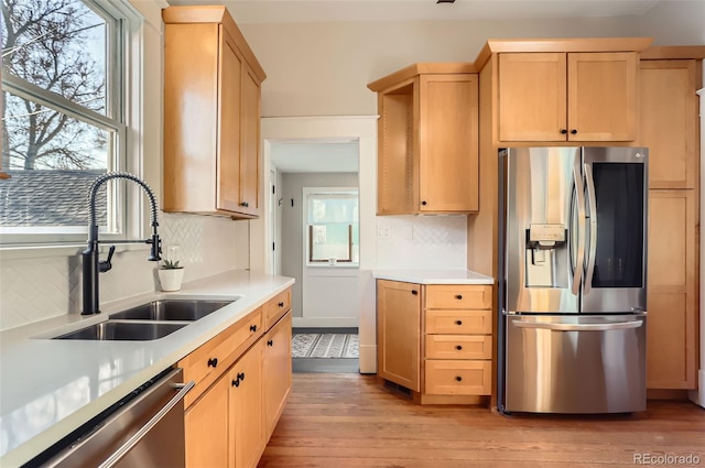 kitchen with light brown cabinetry, light countertops, light wood-style flooring, stainless steel appliances, and a sink