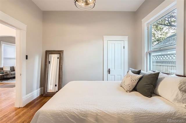 bedroom with arched walkways, baseboards, and wood finished floors