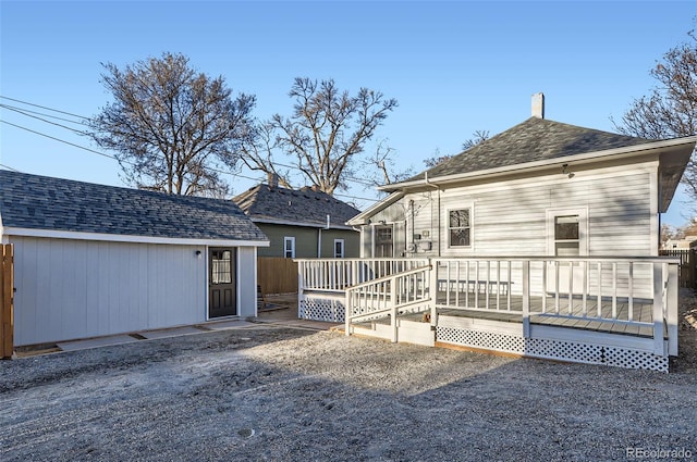 back of property featuring a deck, an outbuilding, and roof with shingles