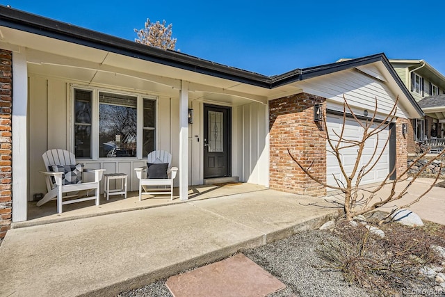 view of exterior entry with a garage, brick siding, a porch, and board and batten siding