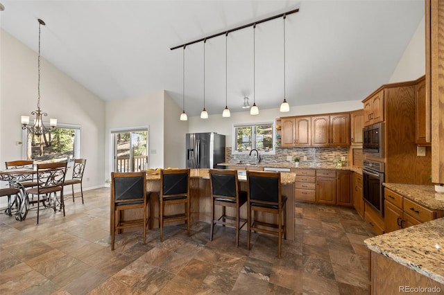 kitchen with appliances with stainless steel finishes, high vaulted ceiling, dark stone finish floors, backsplash, and a chandelier