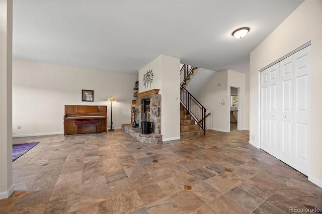 unfurnished living room featuring stairs, stone finish flooring, baseboards, and a stone fireplace
